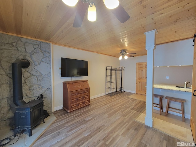 living room with a wood stove, ceiling fan, wooden ceiling, and sink