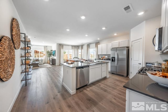 kitchen with a center island with sink, wood-type flooring, white cabinetry, and appliances with stainless steel finishes