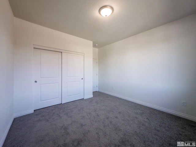 unfurnished bedroom featuring dark colored carpet, a textured ceiling, and a closet