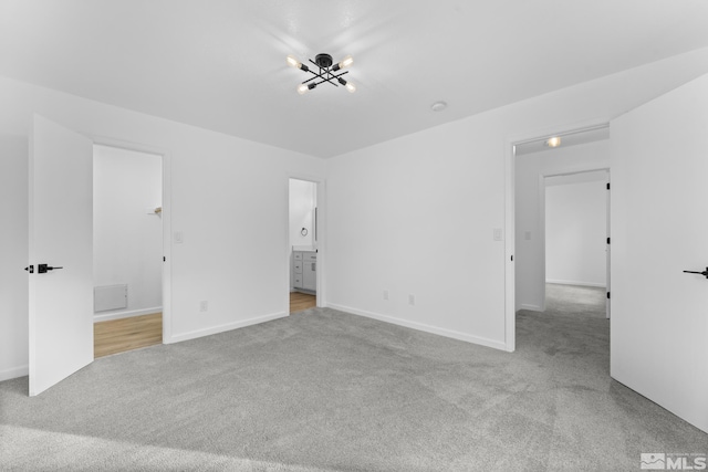 unfurnished bedroom featuring a notable chandelier, ensuite bathroom, and light carpet