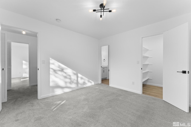 unfurnished bedroom with a spacious closet, a closet, light colored carpet, and ensuite bathroom