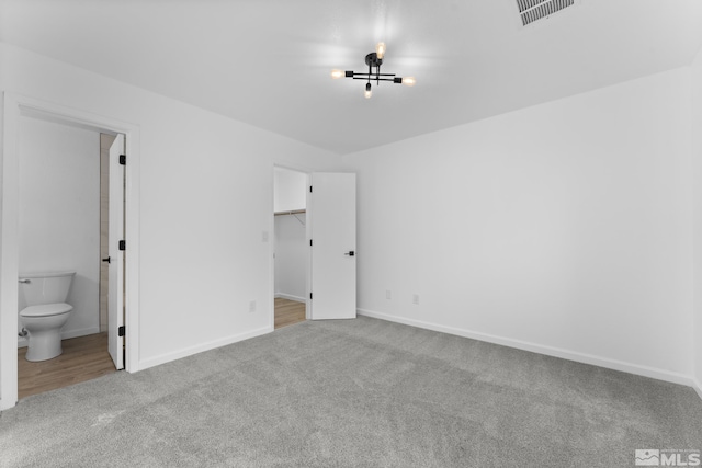 unfurnished bedroom with light carpet, a closet, ensuite bath, and a spacious closet