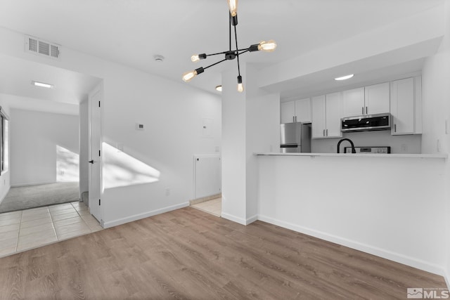 kitchen featuring an inviting chandelier, light hardwood / wood-style flooring, kitchen peninsula, white cabinets, and appliances with stainless steel finishes