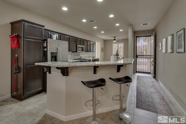 kitchen featuring ceiling fan, light stone countertops, an island with sink, and a breakfast bar area