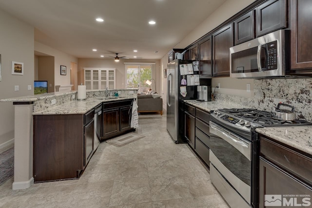 kitchen with light stone countertops, appliances with stainless steel finishes, dark brown cabinetry, ceiling fan, and sink