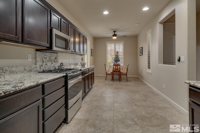 kitchen with backsplash, light stone counters, dark brown cabinets, stainless steel appliances, and ceiling fan