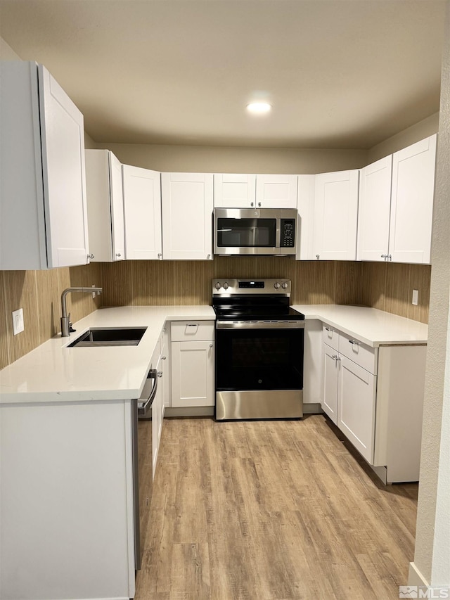 kitchen with white cabinets, sink, light hardwood / wood-style flooring, appliances with stainless steel finishes, and tasteful backsplash