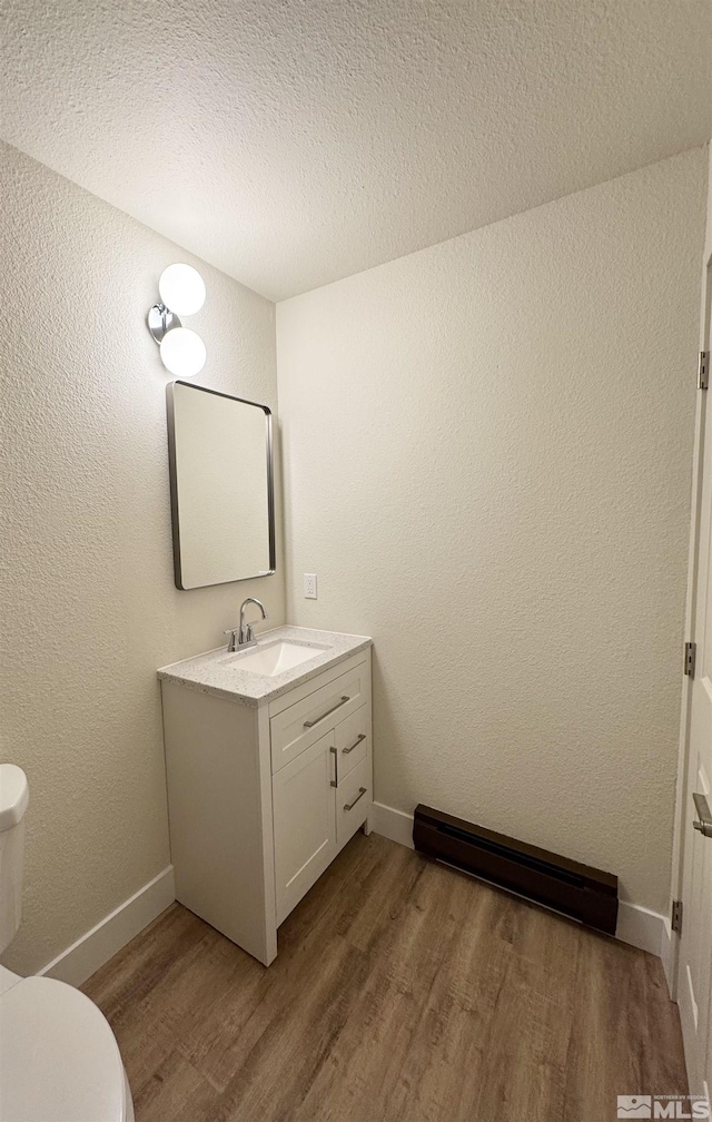 bathroom featuring vanity, toilet, a textured ceiling, a baseboard radiator, and wood-type flooring