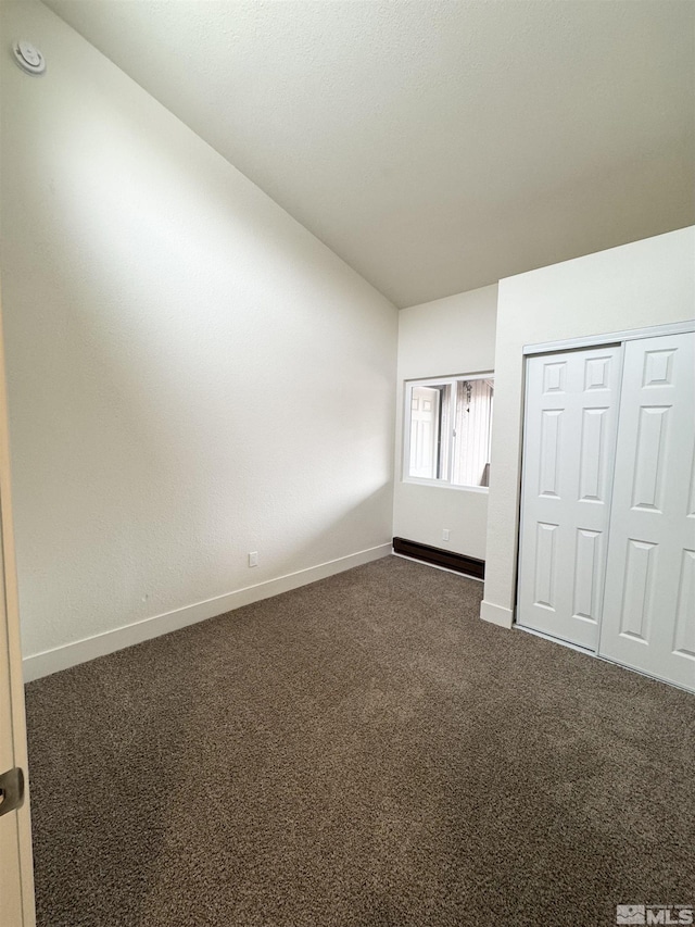 unfurnished bedroom with dark carpet, lofted ceiling, and a closet