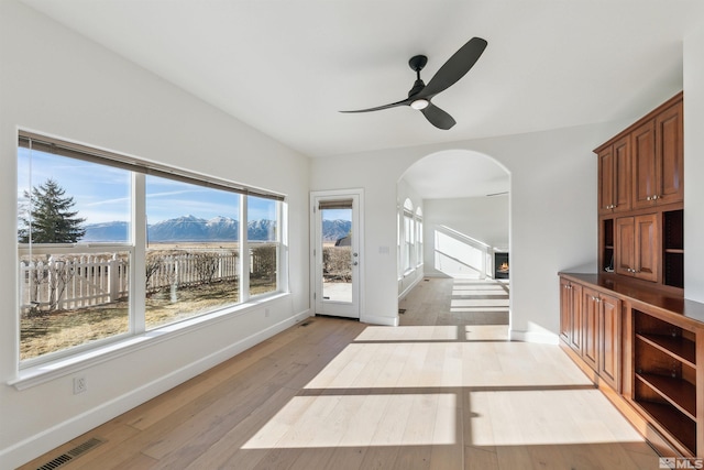 living room with a mountain view, light hardwood / wood-style flooring, ceiling fan, and a healthy amount of sunlight