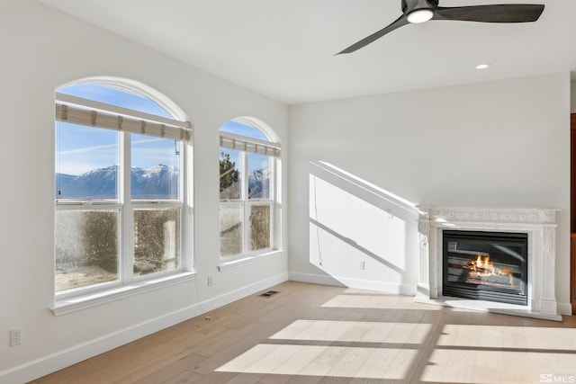 unfurnished living room with a mountain view, plenty of natural light, ceiling fan, and light hardwood / wood-style floors