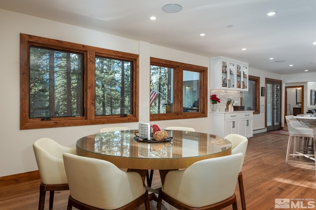 dining area with bar area, hardwood / wood-style floors, and a baseboard heating unit