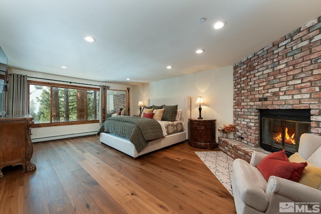 bedroom with hardwood / wood-style floors, a brick fireplace, and a baseboard radiator