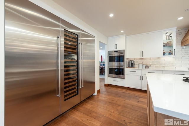 kitchen featuring hardwood / wood-style floors, backsplash, white cabinets, built in refrigerator, and double oven