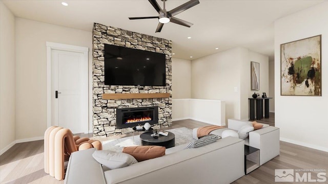 living room with light hardwood / wood-style floors, a stone fireplace, and ceiling fan