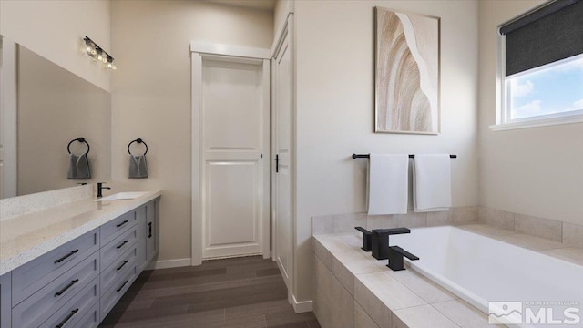 bathroom with hardwood / wood-style floors, vanity, and a relaxing tiled tub