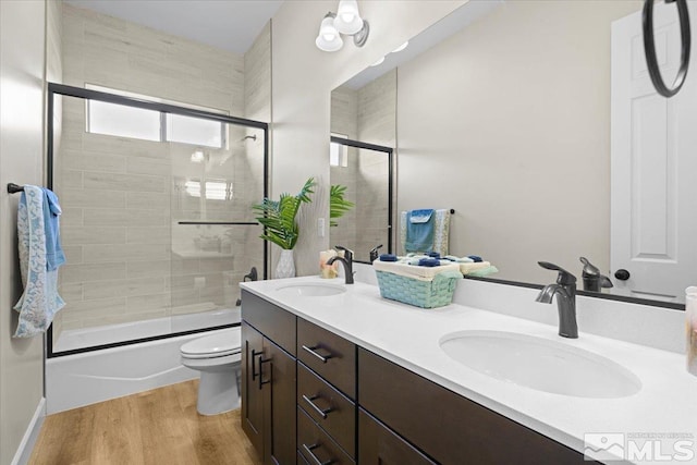 full bathroom featuring hardwood / wood-style flooring, vanity, toilet, and shower / bath combination with glass door