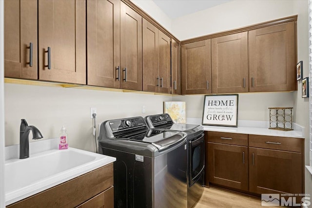 clothes washing area with washer and dryer, light hardwood / wood-style floors, cabinets, and sink