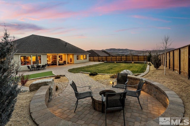 patio terrace at dusk with a fire pit, a mountain view, and a yard