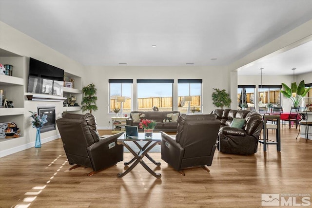 living room featuring a chandelier, built in shelves, and light wood-type flooring