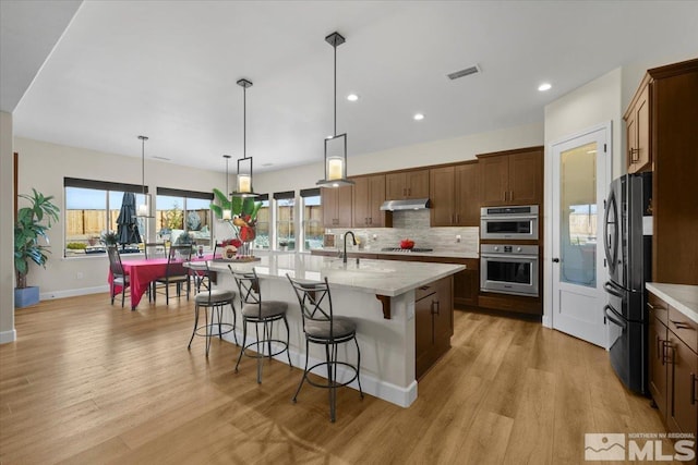 kitchen with pendant lighting, a kitchen breakfast bar, an island with sink, appliances with stainless steel finishes, and tasteful backsplash