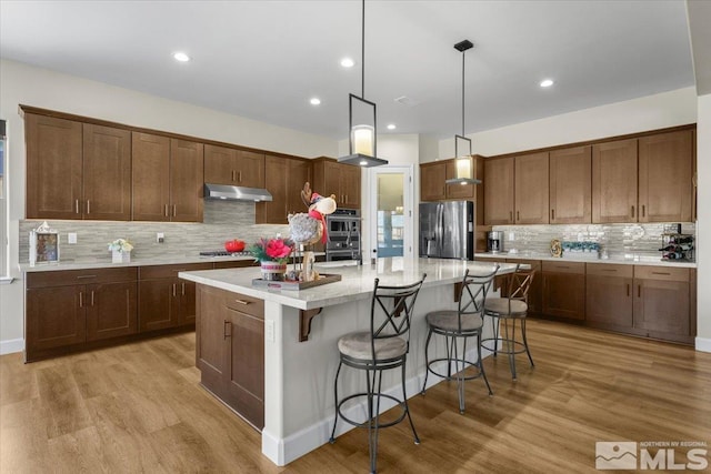 kitchen with a kitchen island with sink, appliances with stainless steel finishes, decorative light fixtures, light hardwood / wood-style floors, and a kitchen bar