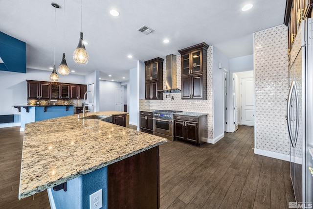 kitchen featuring a center island with sink, sink, wall chimney exhaust hood, decorative backsplash, and appliances with stainless steel finishes