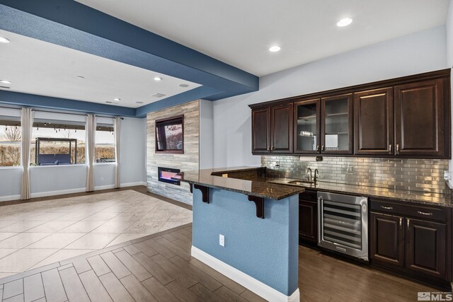 kitchen with a kitchen bar, dark brown cabinetry, dark stone countertops, and beverage cooler