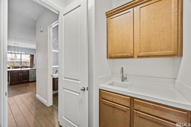 kitchen featuring tile countertops, stainless steel dishwasher, sink, and an inviting chandelier