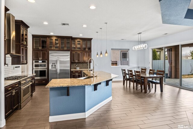 kitchen featuring high end appliances, a kitchen island with sink, a kitchen breakfast bar, sink, and decorative backsplash