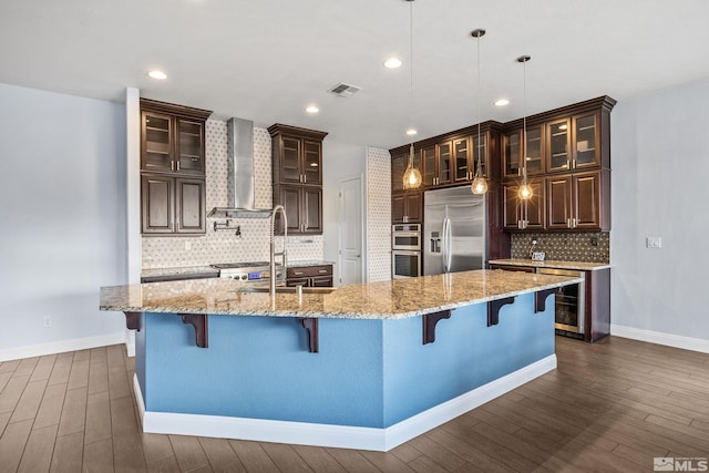 kitchen with a kitchen breakfast bar, a large island with sink, wall chimney range hood, and appliances with stainless steel finishes