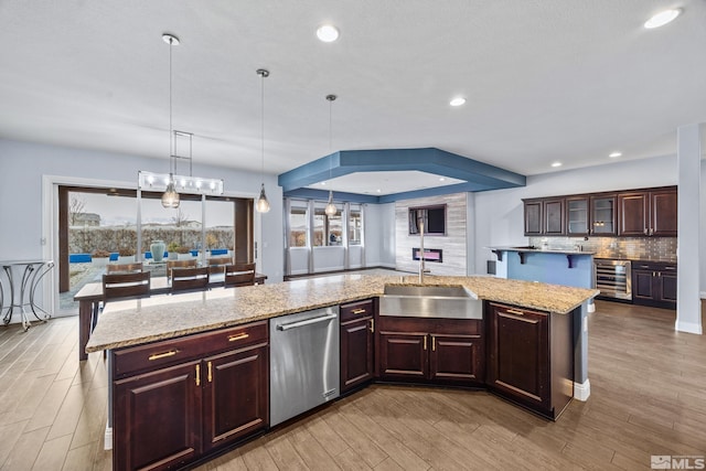 kitchen with a kitchen island with sink, sink, stainless steel dishwasher, decorative light fixtures, and beverage cooler