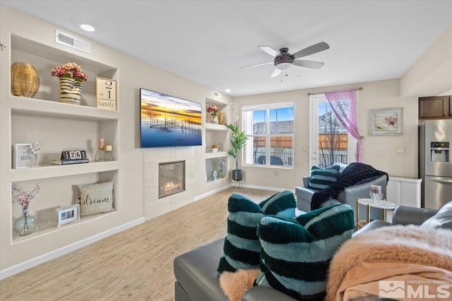 living room featuring a fireplace, light wood-type flooring, built in features, and ceiling fan