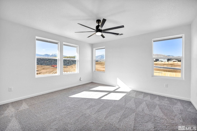 unfurnished room featuring ceiling fan, a mountain view, carpet, and a textured ceiling