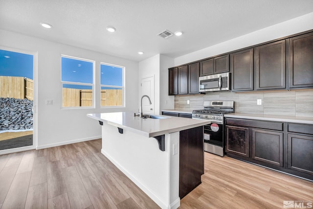 kitchen featuring tasteful backsplash, sink, stainless steel appliances, a center island with sink, and light hardwood / wood-style flooring