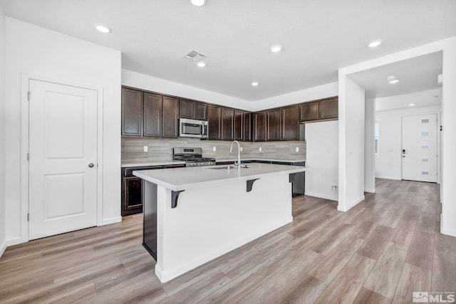 kitchen with appliances with stainless steel finishes, sink, a kitchen island with sink, and dark brown cabinets