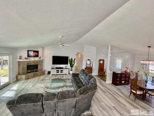 living room featuring ceiling fan with notable chandelier, light hardwood / wood-style floors, lofted ceiling, and a tile fireplace