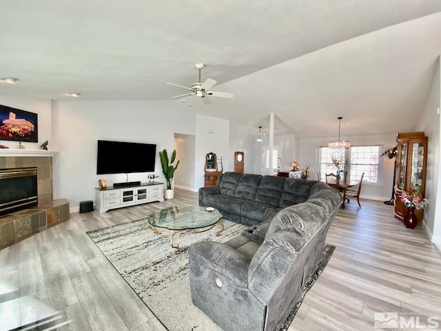 living room with a tile fireplace, ceiling fan with notable chandelier, light hardwood / wood-style flooring, and lofted ceiling