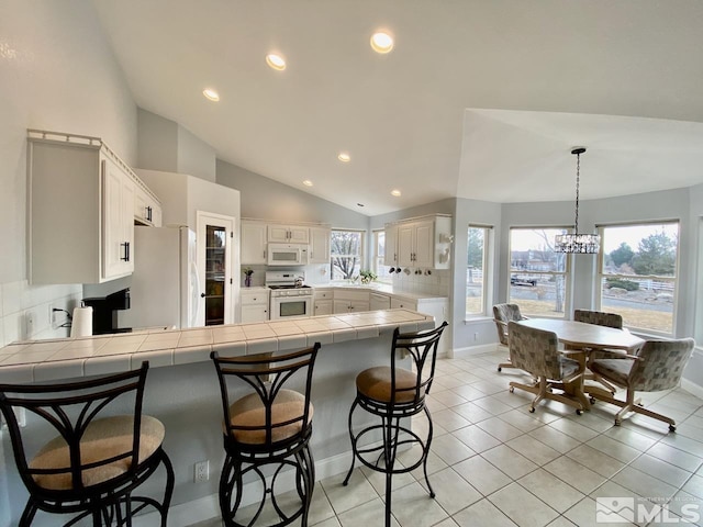 kitchen featuring white appliances, a kitchen breakfast bar, vaulted ceiling, light tile patterned floors, and kitchen peninsula