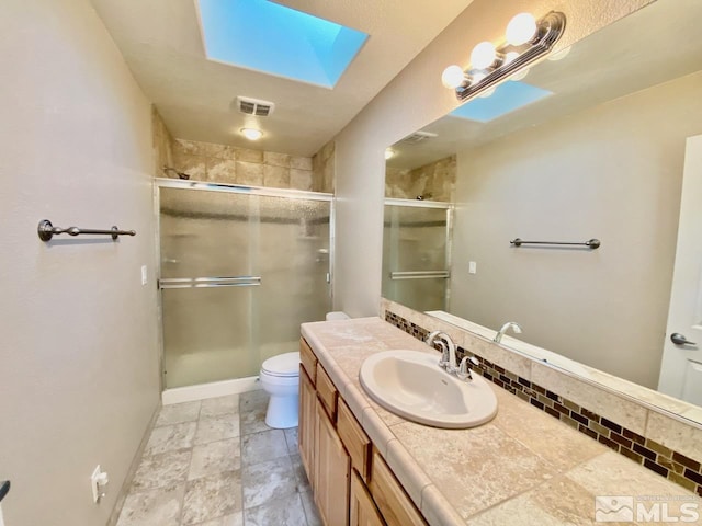 bathroom with vanity, toilet, a shower with shower door, and a skylight