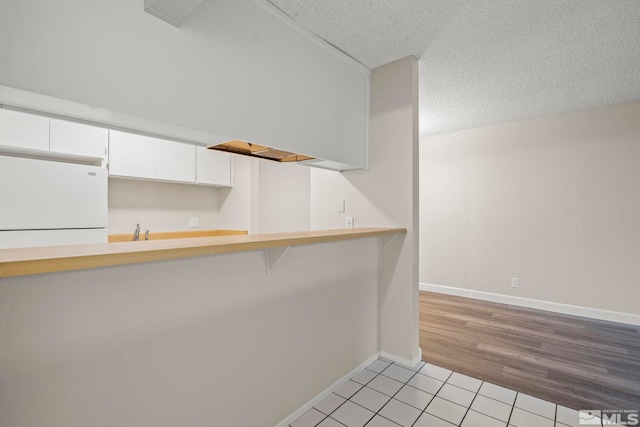 kitchen featuring white cabinets, white refrigerator, light tile patterned floors, and a textured ceiling