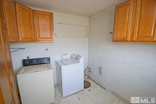 laundry area with cabinets, separate washer and dryer, a textured ceiling, and brick wall