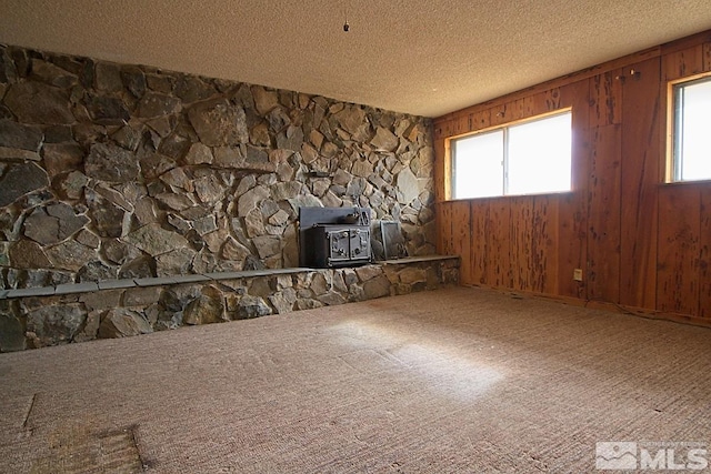 carpeted empty room with a textured ceiling, a wood stove, and wood walls