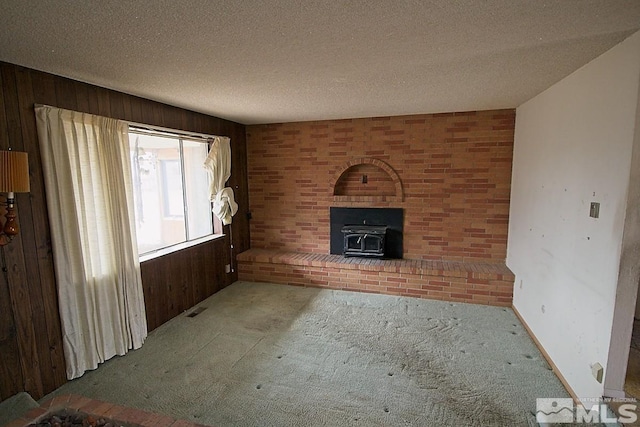 unfurnished living room featuring carpet floors, a textured ceiling, wooden walls, and a wood stove