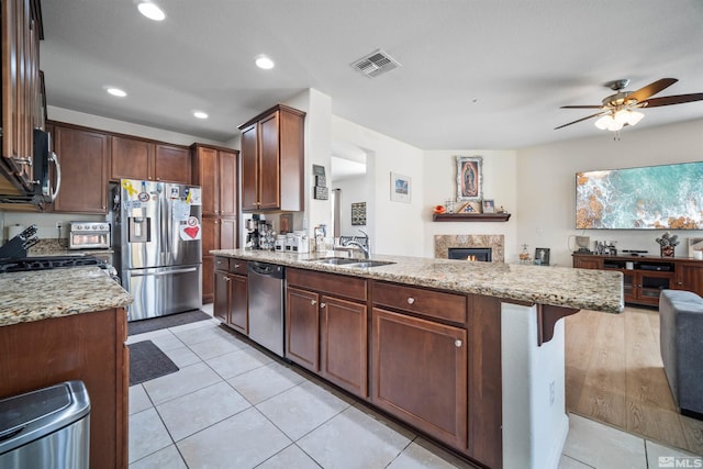 kitchen with appliances with stainless steel finishes, light stone counters, ceiling fan, sink, and light tile patterned flooring