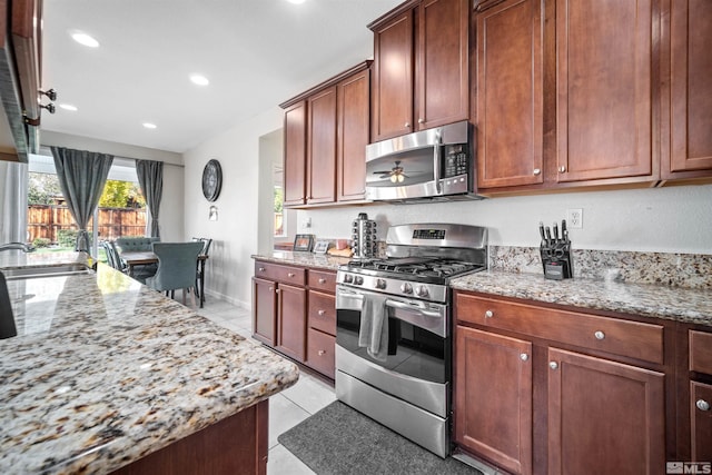 kitchen with sink, ceiling fan, light stone countertops, light tile patterned floors, and stainless steel appliances