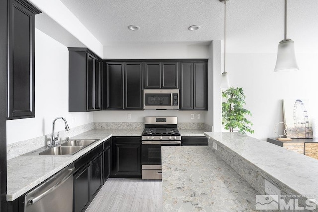 kitchen with a textured ceiling, hanging light fixtures, sink, and appliances with stainless steel finishes