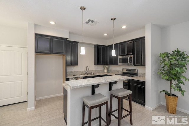 kitchen with a center island, sink, decorative light fixtures, light stone counters, and stainless steel appliances