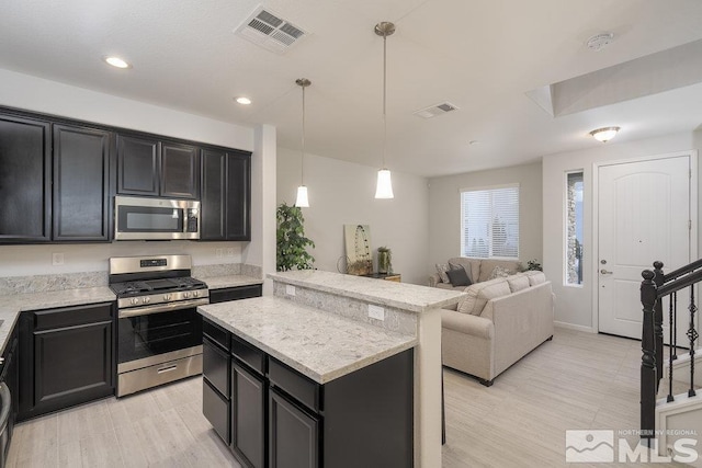 kitchen with stainless steel appliances, light stone counters, decorative light fixtures, a kitchen island, and light wood-type flooring