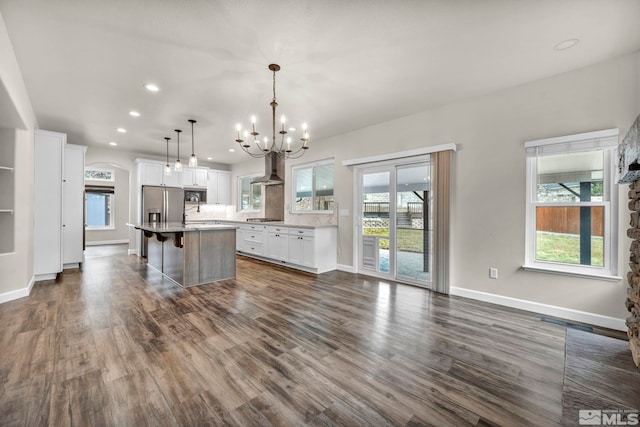 kitchen with appliances with stainless steel finishes, wall chimney exhaust hood, decorative light fixtures, a kitchen island, and a breakfast bar area